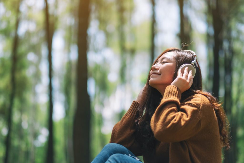 a woman enjoy listening to music with headphone with feeling happy and relaxed in the park