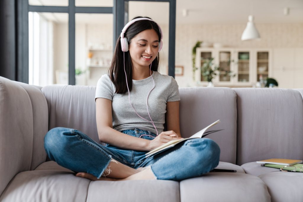 image of happy asian woman using headphones and writing down notes