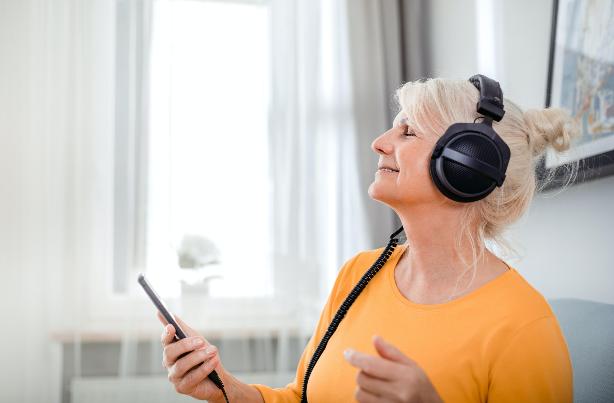 senior woman listening her favourite music at home using headphones and smartphone